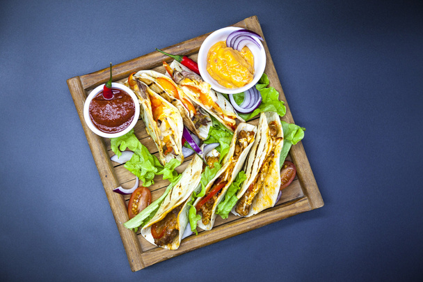 Mexikanische Tortilla mit Fleisch, Rindfleisch und geschmortem Gemüse und würziger Sauce auf einem hölzernen Tablett. - Foto, Bild
