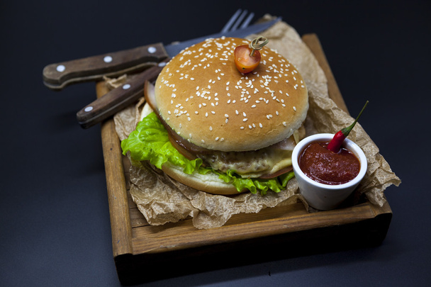 Classical American fresh juicy burger with chicken and ham on a wooden tray with a spicy chili sauce. Beautiful photo on a dark background - Photo, Image