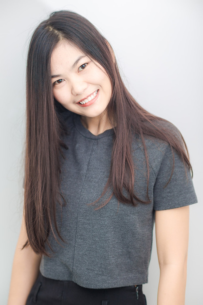 Бережная азиатка улыбается на сером фоне студии
 - Фото, изображение