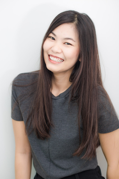 Аккуратная азиатская девушка улыбается на сером фоне студии в гостиной
 - Фото, изображение