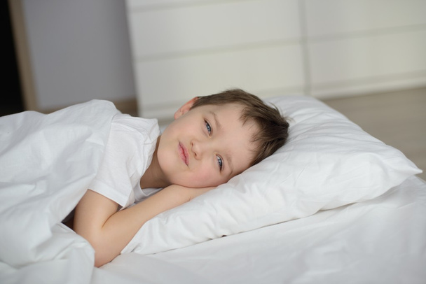 Jongetje rusten in witte bed met ogen open - Foto, afbeelding