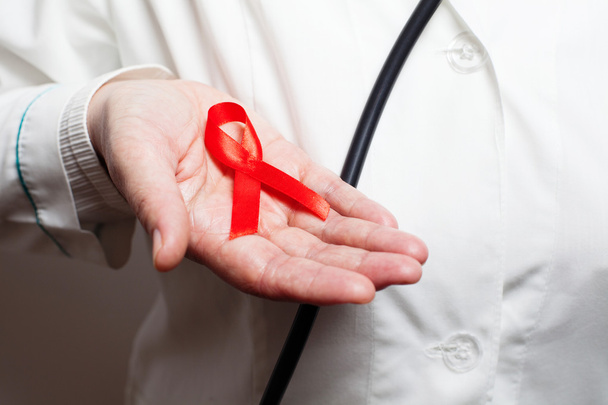 Medic holding red AIDS awareness ribbon on her hand - Fotoğraf, Görsel