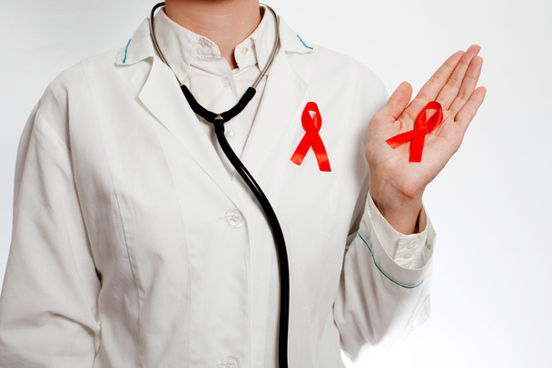 Medic with red AIDS awareness ribbon on her chest holding red AIDS awareness ribbon on her hand - Valokuva, kuva