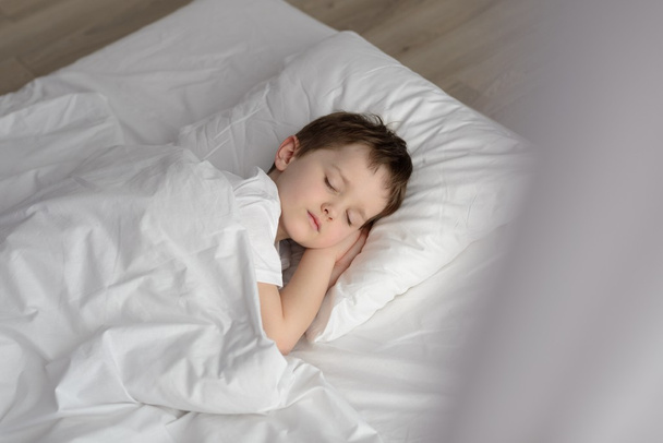 Menino adorável dormindo na cama, hora de dormir feliz no quarto branco
 - Foto, Imagem