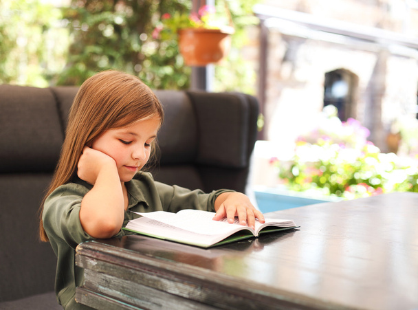 Портрет очаровательной маленькой девочки, читающей книгу в саду
 - Фото, изображение