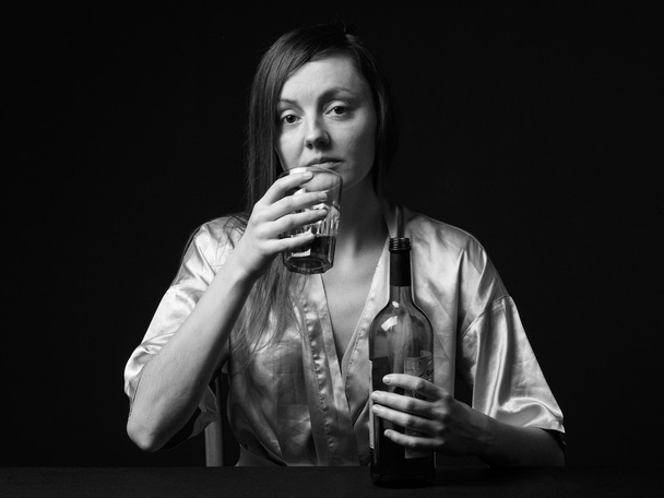 Алкоголизм. Молодая женщина хранит бутылку и бокал вина
 - Фото, изображение