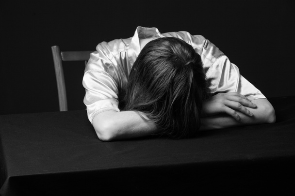 Απελπισία. Γυναίκα είναι ξαπλωμένη στο τραπέζι, κεφάλι στα χέρια - Φωτογραφία, εικόνα
