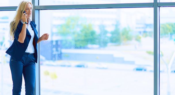 Businesswoman standing against office window talking on mobile phone - Valokuva, kuva