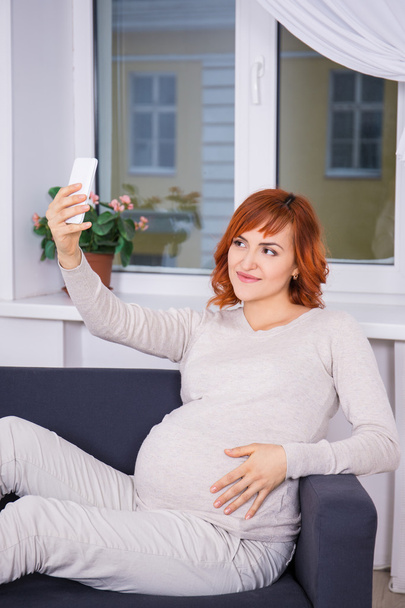 young pregnant woman taking selfie photo with smart phone in liv - Photo, Image