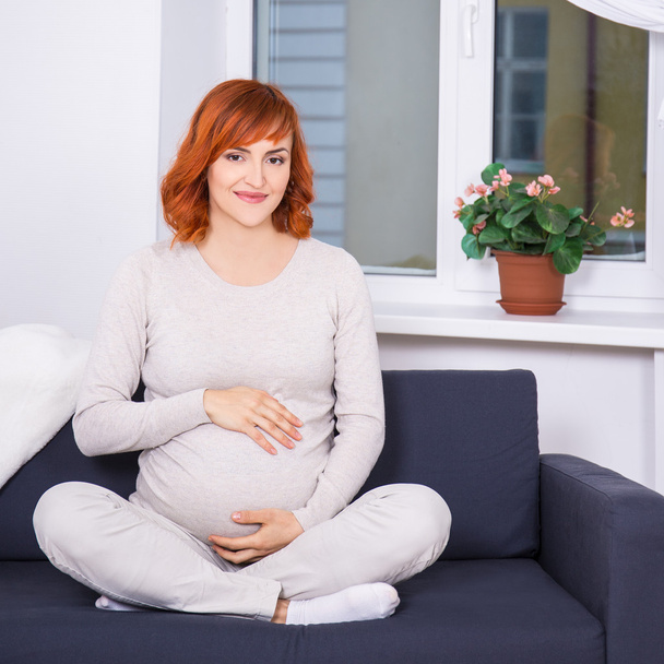 portrait of young pregnant woman sitting in living room - Fotó, kép