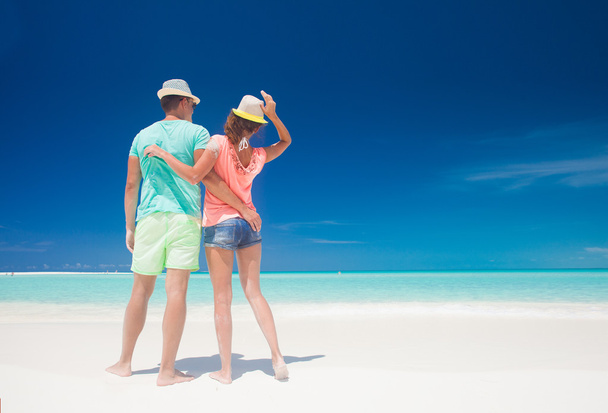 πίσω όψη του ζευγάρι σε φωτεινά ρούχα και καπέλα διασκεδάζουν στην τροπική παραλία - Φωτογραφία, εικόνα