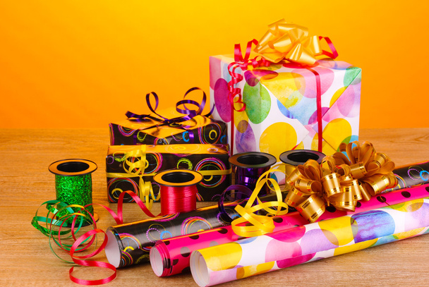 Gigts, paper, ribbon and bows on wooden table on yellow background - 写真・画像