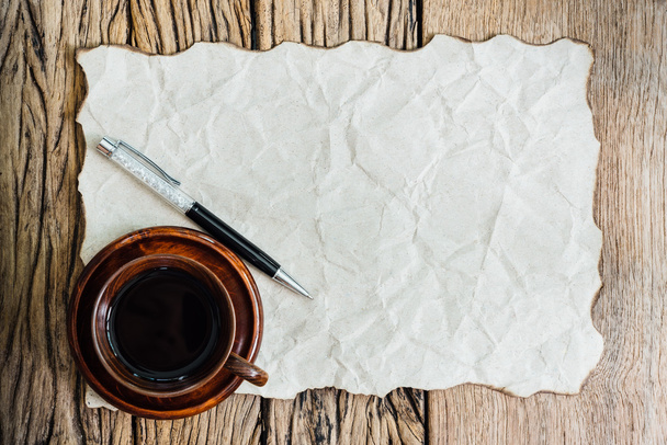 Papel quemado en blanco con bolígrafo y taza de café en mesa de madera vieja
. - Foto, Imagen