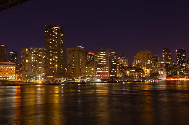 夜のイースト ・ リバーでカラフルな反射とマンハッタンの高層ビル. - 写真・画像