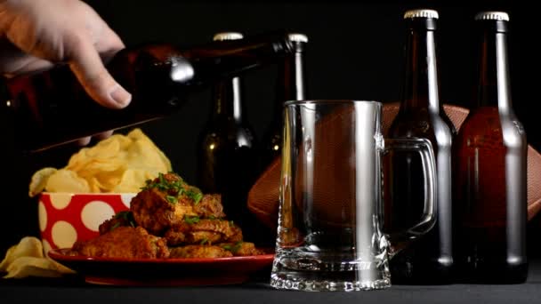 Mano masculina vertiendo cerveza en el vaso de stein con fútbol americano, comida para picar y botellas de cerveza
. - Imágenes, Vídeo