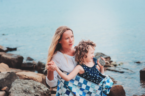 happy mother and daughter wrapped in quilt blanket spending time together on the beach on summer vacation. Happy family traveling, cozy mood. - Fotoğraf, Görsel