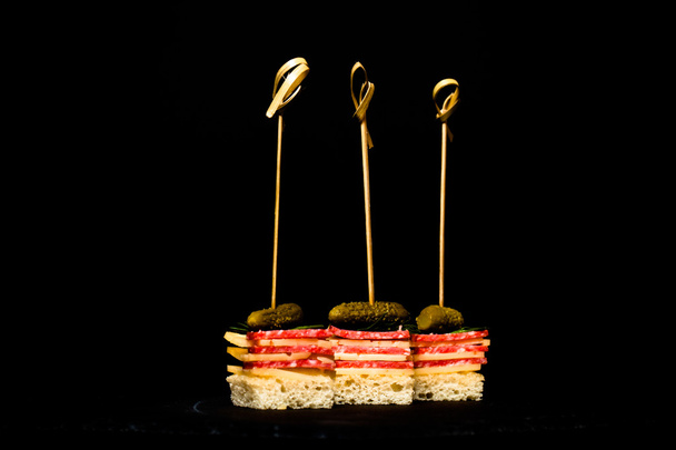 Small snacks canape with salami, cheese and pickle on skewer on  - Foto, afbeelding