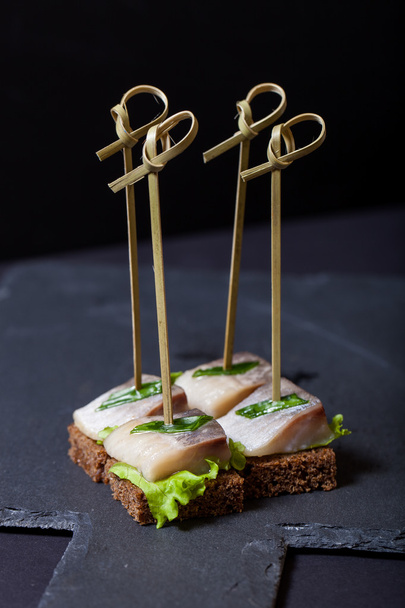 Small snacks canape with herring, rye bread, lettuce and green o - Фото, изображение
