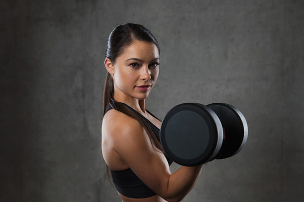 young woman flexing muscles with dumbbells in gym - Photo, Image
