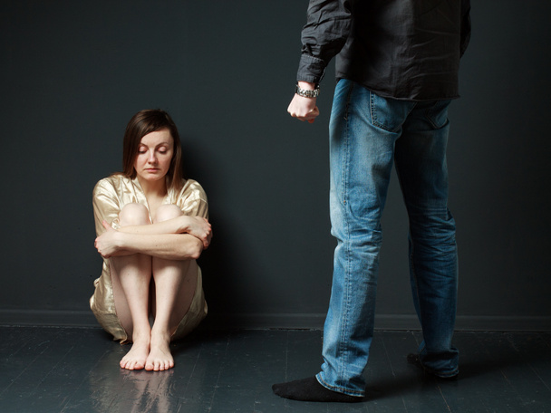 Surullinen nainen istuu lattialla, seisoo miehen hahmo uhka
 - Valokuva, kuva