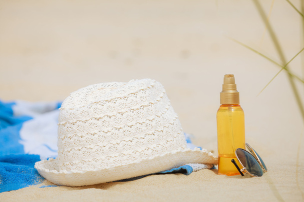 Beach set hat and sunscreen lotion lying on sand - Фото, изображение
