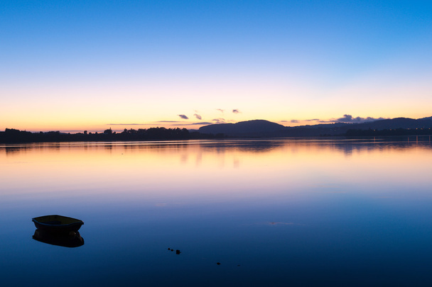 Sunrise için pembe ve turuncu ufuk yukarıda koyu mavi gökyüzü geçişler ve sakin su. - Fotoğraf, Görsel