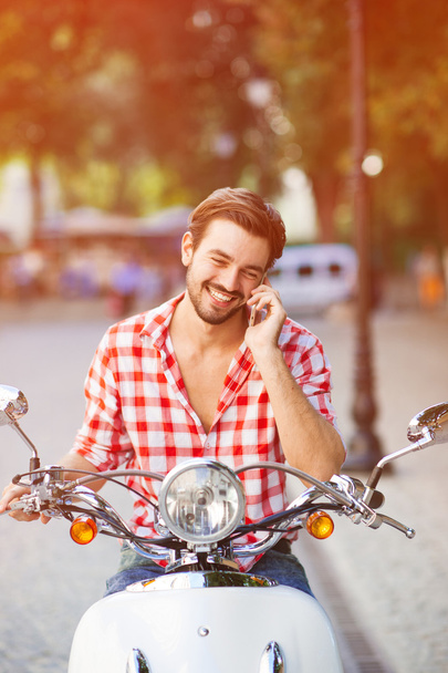 Hadsome young man smiling on a scooter - 写真・画像