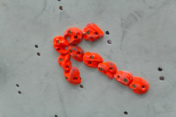 Красное скалолазание выполнено в форме стрелки на серой стене - Фото, изображение