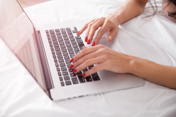 Primer plano de las manos de la mujer con el ordenador portátil en la cama
 - Foto, imagen