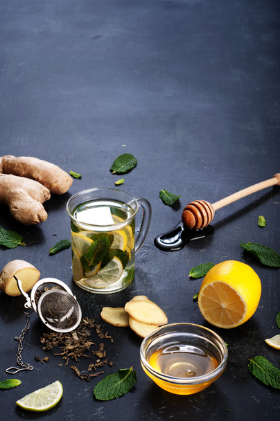 Tea with mint, lime, lemon and ginger on a dark background. Beside the ingredients for tea, such as chopped ginger root, peppermint leaves, slices of lemon and lime. The concept of treatment of colds, without the use of pills and medicines - Fotografie, Obrázek