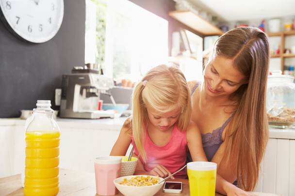 Mother And Daughter Using Mobile Phone At Breakfast Table - Foto, Bild