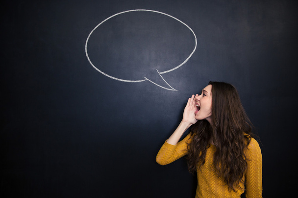 Charming woman screaming against background of chalkboard with speech bubble - Photo, image