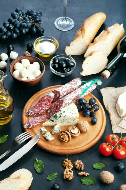 Italian food concept. Jerked sausage, various cheeses, blue grapes, vegetables and fruits on a dark background. - Foto, afbeelding