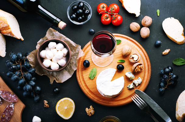 Italian food concept. Jerked sausage, various cheeses, blue grapes, vegetables and fruits on a dark background. - Fotoğraf, Görsel