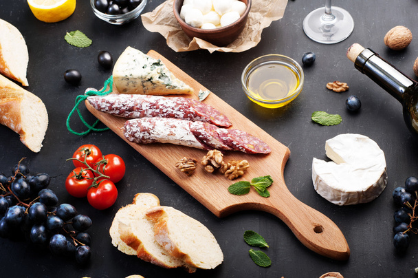Italian food concept. Jerked sausage, various cheeses, blue grapes, vegetables and fruits on a dark background. - Fotó, kép