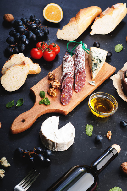 Italian food concept. Jerked sausage, various cheeses, blue grapes, vegetables and fruits on a dark background. - Foto, afbeelding