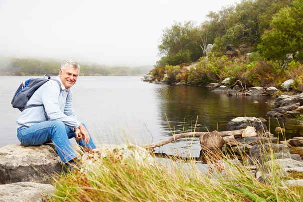 Smiling senior man sitting by a lake - Photo, image