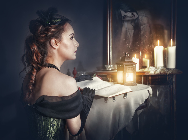 Femme avec livre en robe rétro et fantôme dans le miroir
 - Photo, image