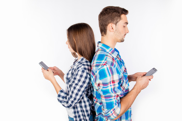 Two lovers standing back to back and typing message on phones - Foto, Imagen