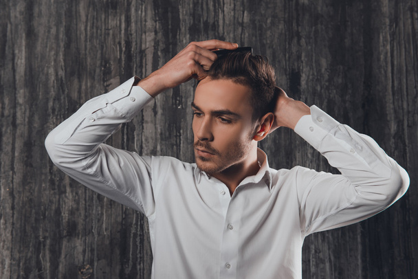Attractive rigid man combing hair on the grey background - Фото, изображение