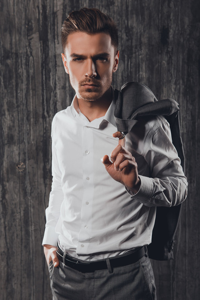 Attractive rigid man holding jacket on a shoulder on the grey ba - Fotografie, Obrázek
