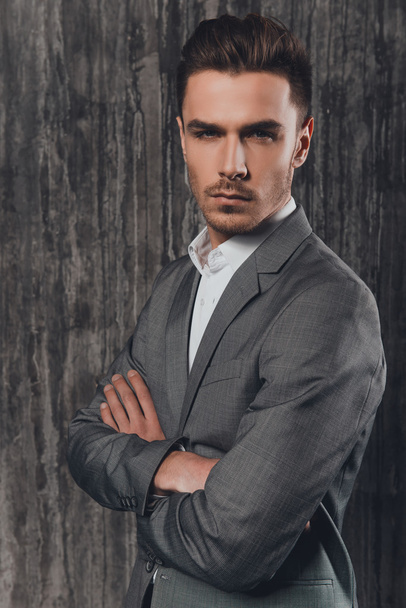 Handome brutal man in suit on the grey background crossing hands - Fotografie, Obrázek