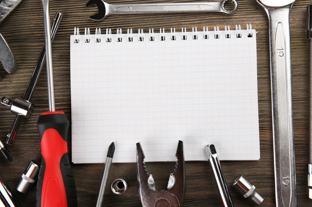 Different kinds of tools with a notebook on wooden background, closeup - Foto, afbeelding