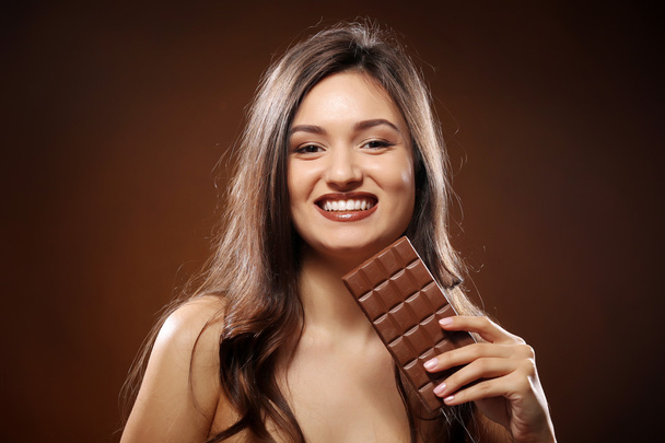 Portrait of attractive young woman with chocolate on brown background, close up - Φωτογραφία, εικόνα