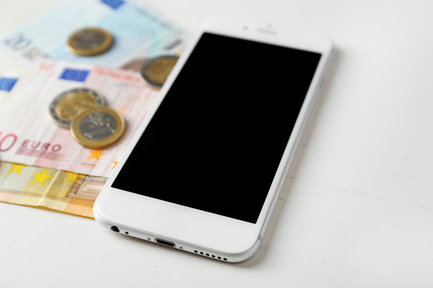 Smart phone and euro banknotes with coins on light table. Telephone charges - Foto, afbeelding