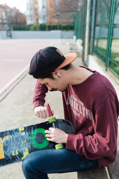 Человек исправляет свой скейт
 - Фото, изображение