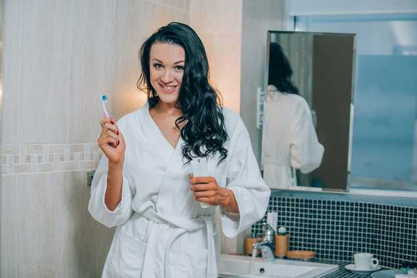 Retrato de mujer atractiva cepillándose los dientes en el baño una capa blanca. dientes sanos
. - Foto, Imagen
