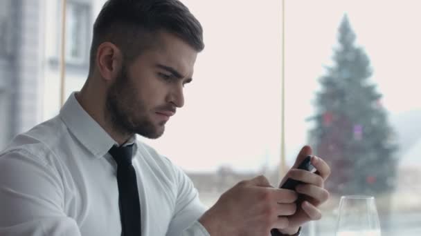 Χαρούμενος νεαρός άνδρας βιαστικά Διαδίκτυο στο smartphone που κάθεται σε καφετέρια - Πλάνα, βίντεο
