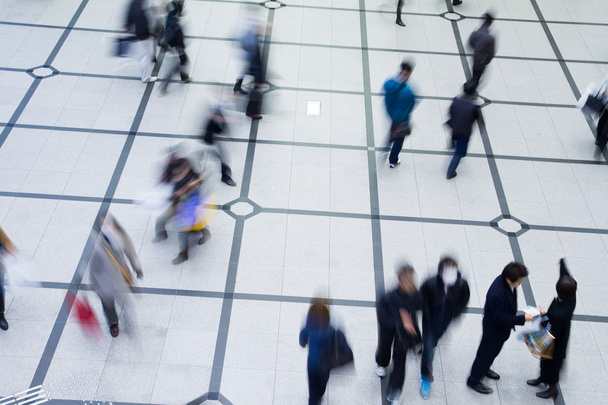 Visão de cima para baixo de grupos de pessoas desfocadas não identificáveis andando e de pé em azulejos em forma de grade sobre o chão
 - Foto, Imagem