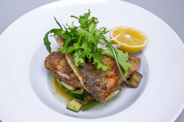 Готовая рыба Дорадо с овощами и лимоном в белой тарелке
 - Фото, изображение